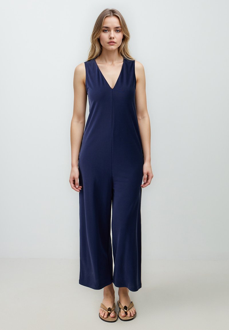 Tutina senza maniche blu navy con scollatura a V, gambe larghe svasate, realizzata in tessuto morbido, con un dettaglio di cucitura centrale.