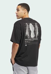 Camiseta de algodón negra con una gran impresión gráfica blanca en la parte posterior, que muestra esquemas de diseño y detalles en texto, de mangas cortas.