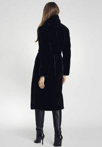 Czarny płaszcz z sztucznego futra z szerokim kołnierzem, długimi rękawami i paskiem w talii. Płaszcz ma miękką teksturę i sięga do połowy łydki.