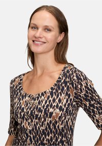 Haut à imprimé léopard avec un décolleté en forme de scoop, des manches courtes et un accent bijou. Fabriqué en tissu texturé dans des tons terreux de marron et de bleu marine.