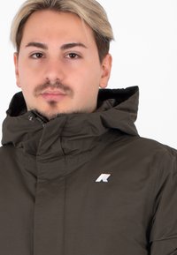 Giacca cappuccio marrone con una texture liscia e chiusura frontale con zip. Presenta un piccolo logo multicolore sul petto.