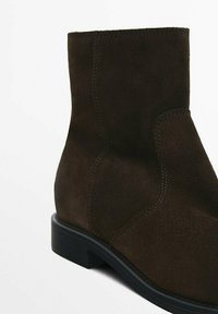 Bottine en daim marron avec un bout arrondi, des coutures minimales et un talon bas noir uni. Présente une texture lisse et un design simple.