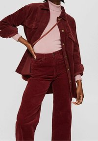 Bordowa kurtka z sztruksu z kieszeniami, w zestawie z jasnoróżowym golfem i pasującymi bordowymi spodniami ze sztruksu o szerokich nogawkach.