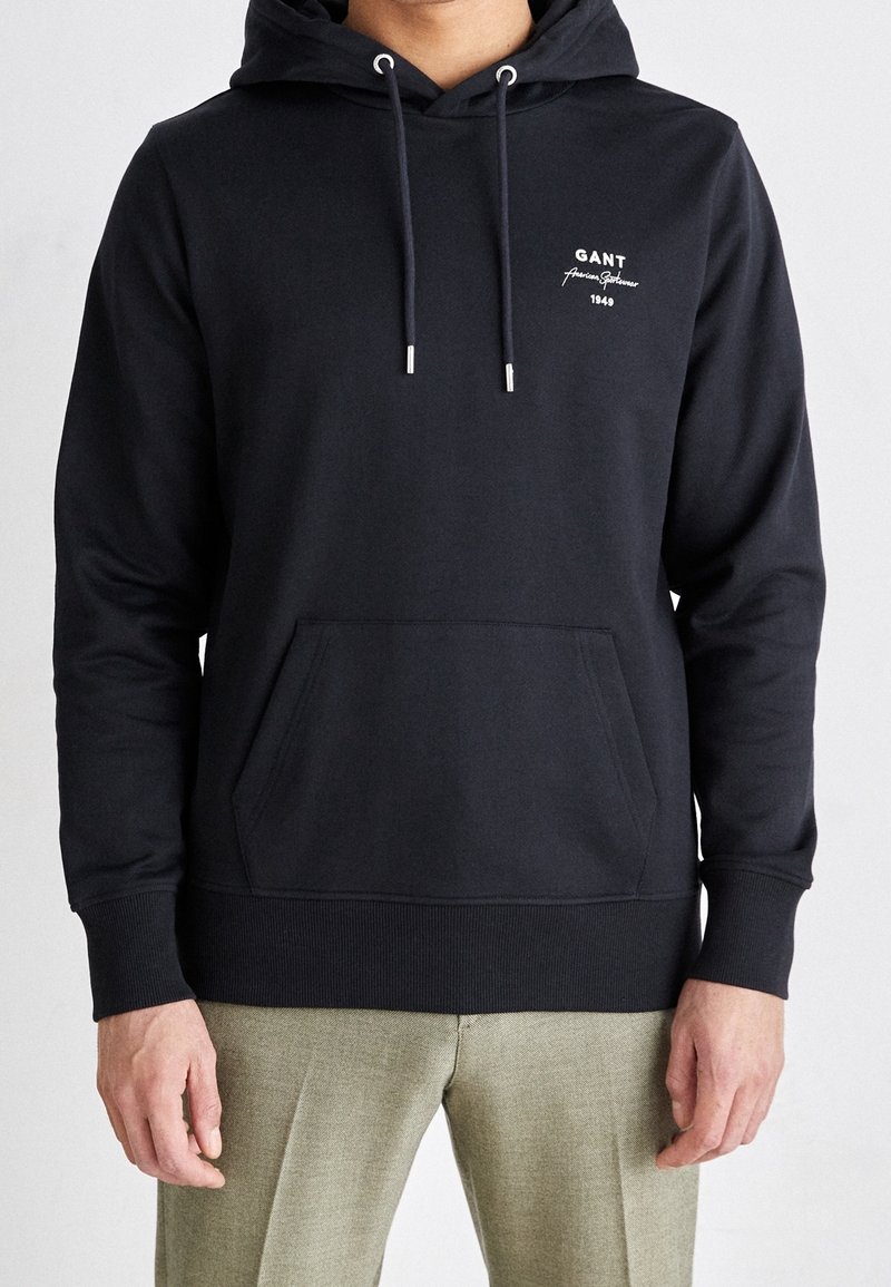 Felpa con cappuccio di un blu scuro, realizzata in un tessuto misto cotone, con tasca frontale, cordino regolabile, ricamo del logo bianco e polsini a costine.