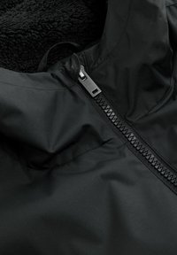 Czarna kurtka z gładką powierzchnią, podszyta fleece, z przodem na zamek błyskawiczny z metalowymi elementami w kolorze srebrnym oraz stojącym kołnierzem.