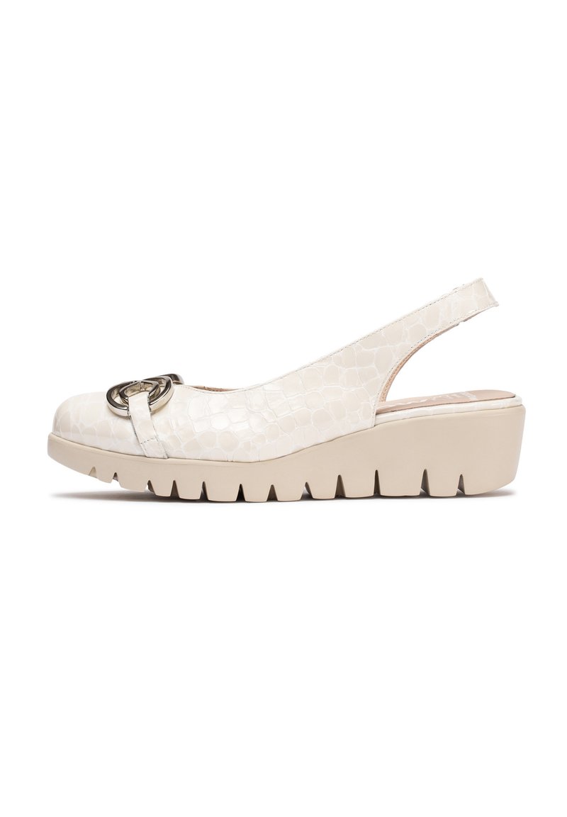 Zapato de cuña tipo slingback en material texturizado beige con un acabado suave. Presenta un acento metálico circular y una suela de plataforma estriada.