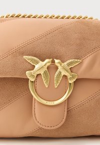 Clutch in pelle e suede color cuoio, con un anello in tono oro con due accenti a forma di uccello, una finitura texturizzata e una chiusura a zip con hardware dorato.