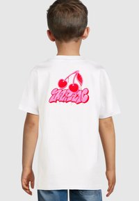 T-shirt bianca con un design grafico rosa di due ciliegie e testo stilizzato sul retro. Maniche corte e vestibilità standard.