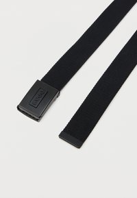 Czarny pleciony pasek materiałowy z prostokątną czarną klamrą z napisem "HUGO" na białym tle.