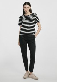 Czarny i biały w paski krótki rękaw T-shirt z okrągłym dekoltem, w zestawie z czarnymi spodniami i beżowymi sneakersami. Posiada mały detal z logo.