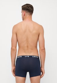 Sötétkék boxeralsó, puha textúrával, fekete derékszíjjal, amelyen a "Levi's" felirat található. A modell hátulról látható, mezítelen törzzsel.