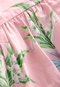 Material roz cu imprimeu floral cu lăcrămioare verzi și albe și detaliu cu cusături strânse.