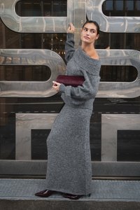Grauer gestrickter Pullover mit schulterfreiem Design, kombiniert mit einem passenden langen Rock. Dunkelburgunderfarbene Clutch und lackierte spitze Pumps.