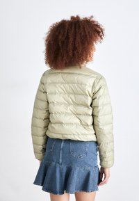 Lys olivengrønn pufferjakke med horisontal quiltet tekstur, myk finish og et enkelt design, kombinert med et denimskjørt med volangkant.