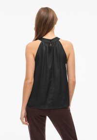 Black satin sleeveless top with a high neck, pleated back detail, and keyhole button closure, paired with dark brown pants.