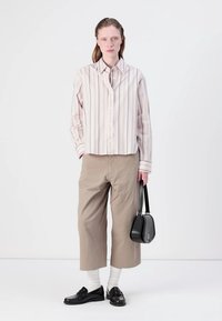 Stripete skjorte i lys rosa og hvit, sammen med løse beige capribukser. En svart veske og loafers fullfører antrekket.