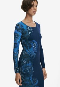 Blaues Langarmkleid mit floralem Muster in verschiedenen Blautönen und strukturierter Oberfläche. Rundhalsausschnitt und taillierte Form.