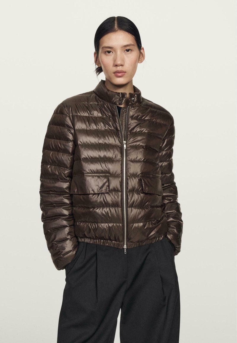 Veste en duvet marron avec un col haut, fermeture éclair à l'avant et texture matelassée. Elle dispose de deux poches avant et d'une coupe légèrement courte.