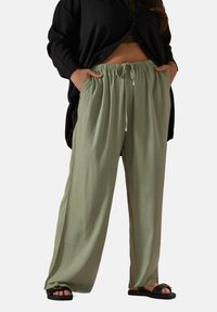 Ljust gröna, vida byxor med elastisk midja och dragsko. Slät textur, tillverkade av andas tyg, kombinerat med svarta sandaler.