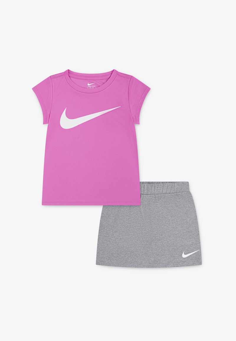Rózsaszín sportpóló fehér Nike logóval, szürke szoknyával párosítva, amely rugalmas derékpánttal és fehér logóakkal rendelkezik. Könnyű anyag.