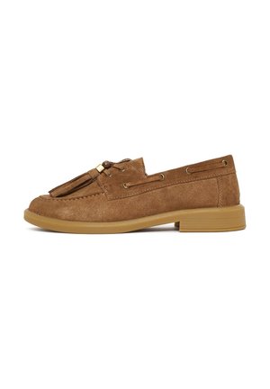 Bruine suède loafer met kwastjes, gouden oogjes en een lage beige rubberen hak, gezien van links op een witte achtergrond.