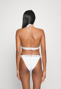 Set di bikini bianco con top a collo alto e chiusura posteriore, e parte inferiore a copertura minima, accentuato da una cintura con logo.