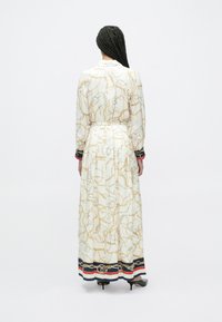 Gara balta kleita ar zelta ķēžu rakstu, garām piedurknēm, jostasvietu un tumši zilu apmali ar sarkaniem un baltiem svītrām.