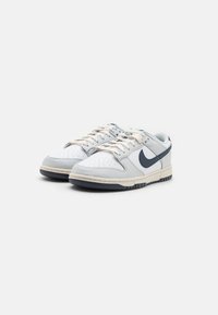 Sneakers in pelle bianca con accenti grigio chiaro e blu navy, dotati di una punta perforata, lacci piatti e una suola in gomma spessa.