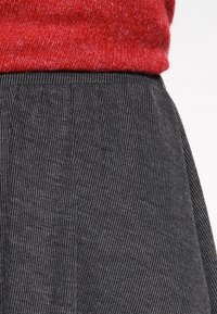 Un pull en tricot rouge porté au-dessus d'une jupe rayée noire et grise, avec des lignes verticales et une silhouette évasée. Texture douce et design ajusté.