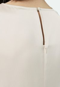 Jasnobeżowa bluzka o gładkiej fakturze, z zapięciem na zamek błyskawiczny z tyłu i subtelnym rozcięciem przy dekolcie. Prosty i minimalistyczny design.