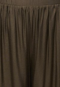 Hnedá tkanina s textúrovaným, krčeným vzhľadom. Obsahuje nariasené záhyby pozdĺž línie pása pre pohodlný strih.