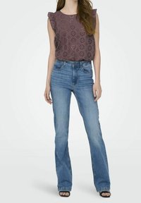 Top viola con occhielli e maniche a volants, abbinato a jeans svasati blu chiaro e sandali neri con tacco.