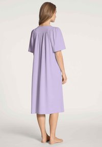 Caminetto lilla con maniche corte, caratterizzato da un corpetto arricciato e una silhouette ampia e fluida che scende sotto il ginocchio. Tessuto dalla texture liscia.