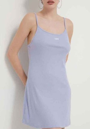 Mujer vistiendo un vestido de tirantes ligero de color púrpura con un pequeño logo blanco en el pecho, de pie contra un fondo liso.