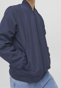 Marynarka bombowa w kolorze granatowym, wykonana z gładkiego, lekkiego materiału, z zamkiem błyskawicznym z przodu, żebrowanym dekoltem oraz elastycznymi mankietami i dołem.