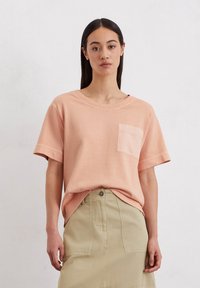 Perzikkleurig katoenen T-shirt met een ronde halslijn, korte mouwen en een enkele borstzak, gecombineerd met een khaki rok. Zachte textuur.