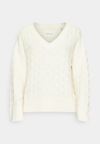 Pull en V en tricot de couleur blanc cassé avec des motifs géométriques, des poignets et un ourlet à côtes. Fabriqué en tissu texturé pour plus de détails et de chaleur.