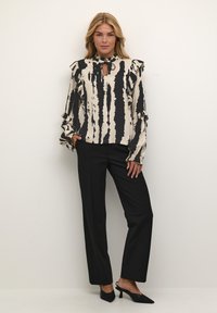 Blusa a righe nere e panna con maniche a balze e scollatura a chiave, abbinata a pantaloni neri a gamba dritta e décolleté con punta.