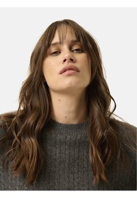 Suéter de punto acanalado gris con cuello redondo, que presenta una textura suave y un diseño ajustado. El modelo tiene el cabello largo y ondulado y un fondo neutro.