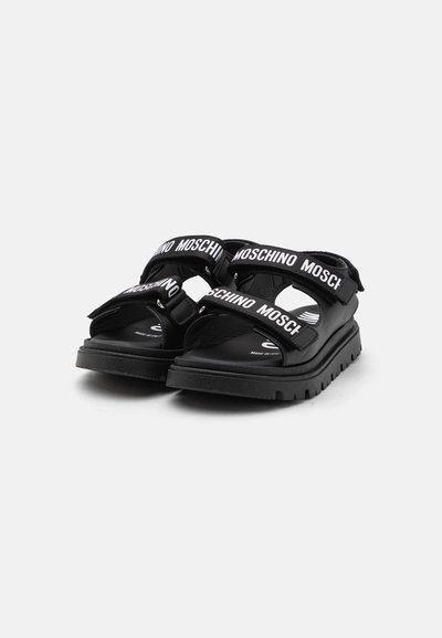 Sandalias negras con correas anchas que presentan la marca "MOSCHINO". Plantillas acolchadas y suelas de goma resistentes. Diseño abierto con cierre ajustable.