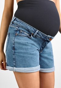 Shorts de maternidad de mezclilla en azul claro, con dobladillo enrollado, bolsillos frontales y un cierre de botón clásico, diseñados para una barriga en crecimiento.