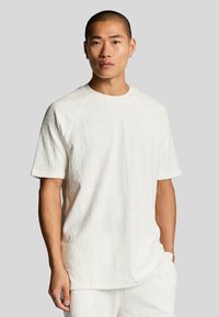 Vit t-shirt med kort ärm som har ett texturerat mönster. Mjuk, plufsig tyg med rundad halsringning och raglan ärmar.