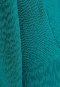 Tissu texturé bleu sarcelle avec des plis verticaux et un léger éclat, présentant un design légèrement froissé.