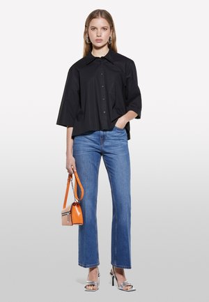 Chemise noire surdimensionnée à manches courtes avec un boutonnage à l'avant, associée à un jean droit bleu clair. Les accessoires comprennent un sac à main orange et des talons argentés.