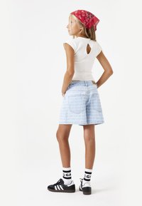 Haut blanc à manches courtes avec découpe dans le dos, short en denim à motifs bleu clair, chaussures noires avec rayures blanches et bandana rouge.