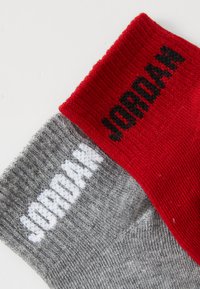 Szürke és piros pamut zoknik, fehér és fekete kötött "JORDAN" felirattal a szárakon. A tetején bordázott textúra.
