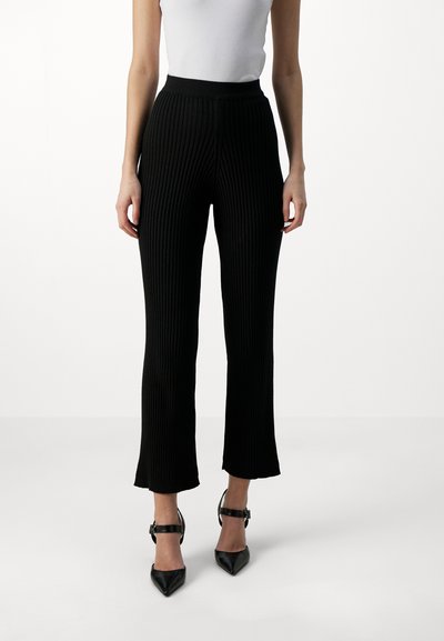 Black ribbed knit trousers with a fitted waist, flared legs ending at mid-calf, paired with black pointed-toe ankle strap heels.
