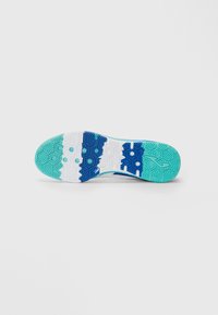 Semelle de chaussure présentant un design texturé avec des segments de couleur turquoise, blanc et bleu, ainsi que des motifs hexagonaux pour une meilleure adhérence.