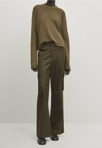 Pull en tricot marron à manches longues, associé à un pantalon cargo vert foncé à jambes larges avec poches latérales et taille ajustée. Sandales noires complètent le look.