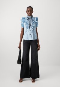 Gaiši zils krekls ar ruche detaļām, augstu apkakli un melnu lentu, apvienots ar platām melnām džinsām un melnu rokassomu. Gluda auduma tekstūra.